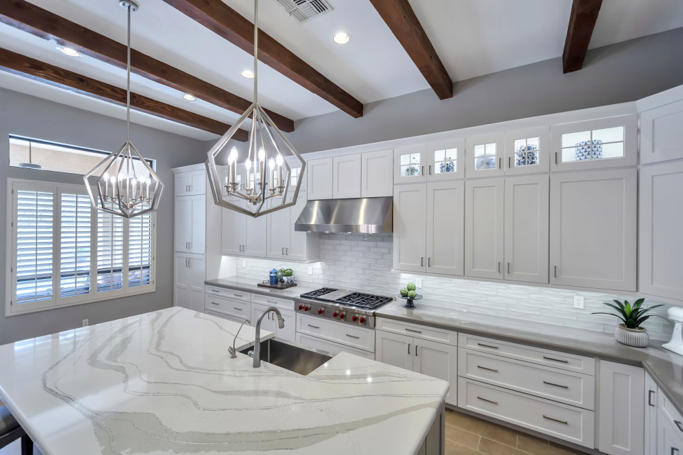 Large transitional u-shaped porcelain tile, beige floor and exposed beam enclosed kitchen photo in Phoenix with a farmhouse sink, shaker cabinets, white cabinets, quartz countertops, white backsplash, glass tile backsplash, stainless steel appliances, an island and white countertops