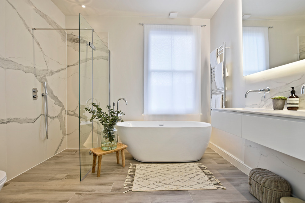 Design ideas for a large beach style master bathroom in London with flat-panel cabinets, white cabinets, a freestanding tub, an open shower, white tile, porcelain tile, wood-look tile, a wall-mount sink, solid surface benchtops, an open shower, a double vanity and a floating vanity.