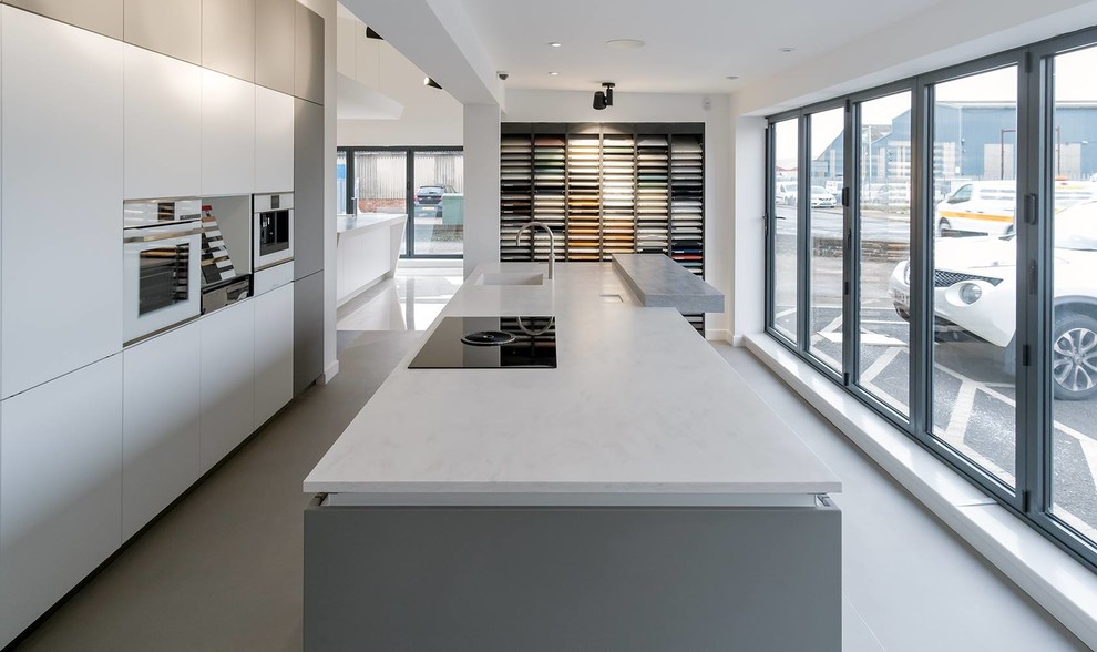 Photo of a large modern single-wall open plan kitchen in Other with an integrated sink, flat-panel cabinets, white cabinets, solid surface benchtops, stainless steel appliances, concrete floors, with island, grey floor and white benchtop.