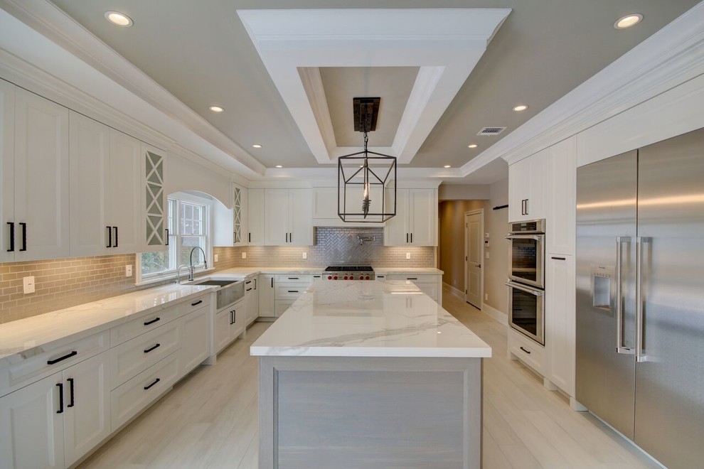 Photo of a large transitional eat-in kitchen in New York with a farmhouse sink, recessed-panel cabinets, white cabinets, quartz benchtops, beige splashback, porcelain splashback, stainless steel appliances, light hardwood floors, with island and grey floor.