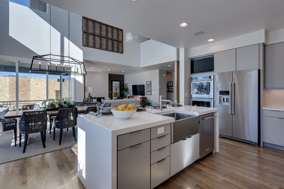 This is an example of a midcentury u-shaped eat-in kitchen in Denver with a farmhouse sink, flat-panel cabinets, grey cabinets, quartz benchtops, white splashback, mosaic tile splashback, stainless steel appliances, light hardwood floors and with island.