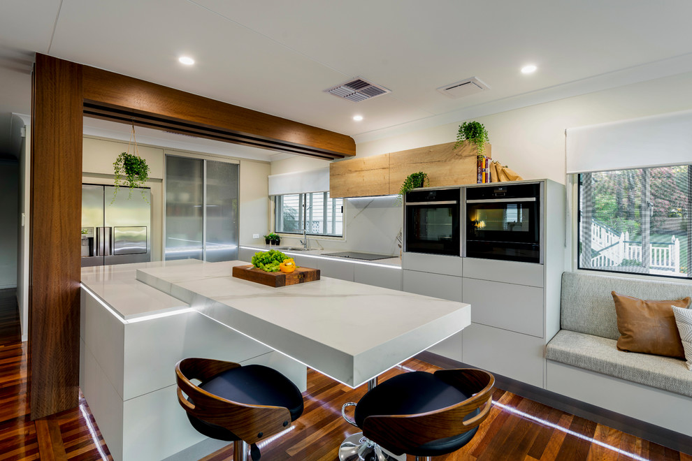 Inspiration for a large contemporary l-shaped eat-in kitchen in Brisbane with an undermount sink, flat-panel cabinets, beige cabinets, quartz benchtops, white splashback, stone slab splashback, black appliances, medium hardwood floors, with island, multi-coloured floor and yellow benchtop.