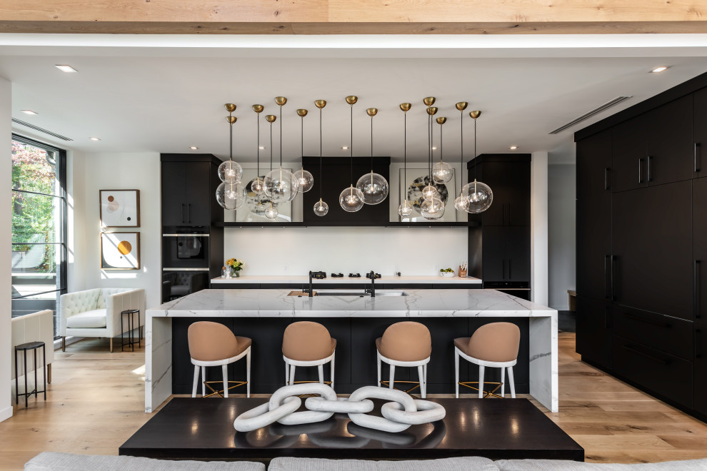 Large contemporary l-shaped open plan kitchen in Other with an undermount sink, flat-panel cabinets, black cabinets, white splashback, panelled appliances, light hardwood floors, with island, brown floor and white benchtop.