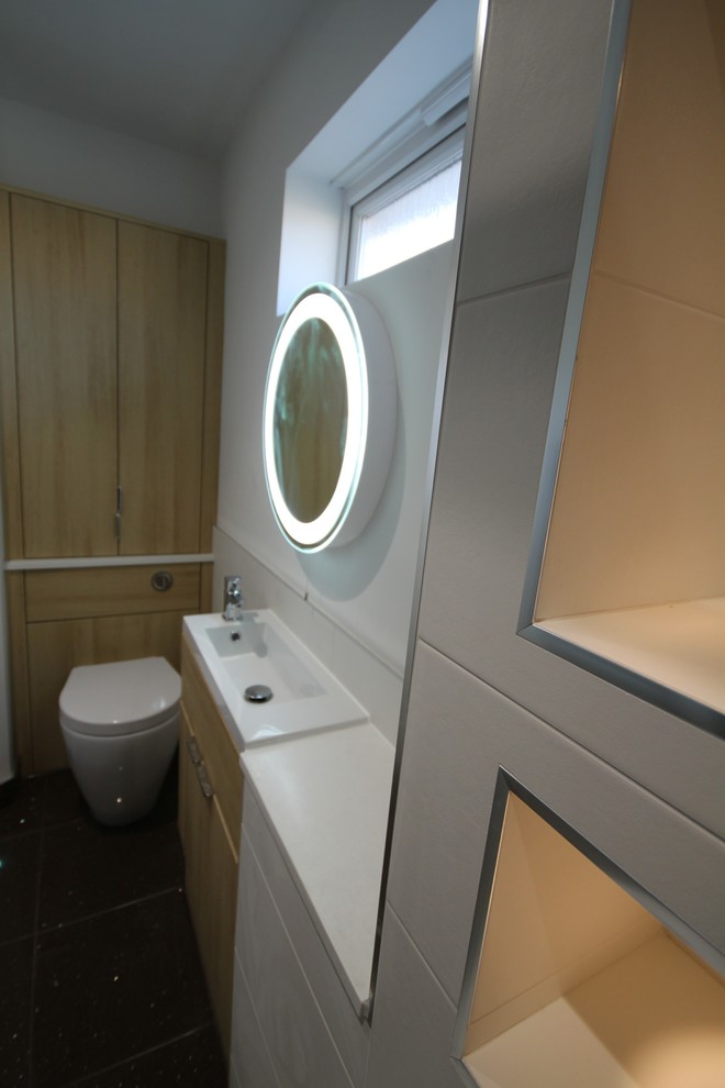 This is an example of a contemporary kids bathroom in Cardiff with flat-panel cabinets, light wood cabinets, a double shower, a wall-mount toilet, white tile, ceramic tile, white walls, a drop-in sink and solid surface benchtops.