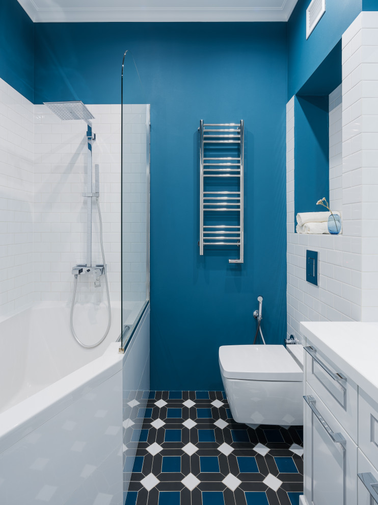 Design ideas for a mid-sized kids bathroom in Other with recessed-panel cabinets, white cabinets, a freestanding tub, an alcove shower, a wall-mount toilet, white tile, ceramic tile, blue walls, porcelain floors, an undermount sink, solid surface benchtops, blue floor, a hinged shower door, white benchtops, a single vanity, a floating vanity and wallpaper.