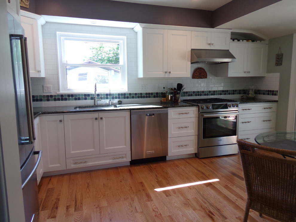 Example of a mid-sized transitional l-shaped light wood floor enclosed kitchen design with an undermount sink, flat-panel cabinets, white cabinets, granite countertops, white backsplash, subway tile backsplash, stainless steel appliances and no island