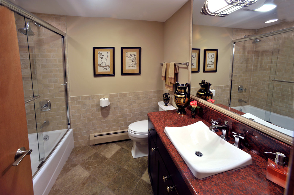 Photo of a mid-sized traditional 3/4 bathroom in Milwaukee with a drop-in sink, recessed-panel cabinets, dark wood cabinets, granite benchtops, a shower/bathtub combo, beige tile, ceramic tile, a one-piece toilet, beige walls, porcelain floors, a sliding shower screen and red benchtops.