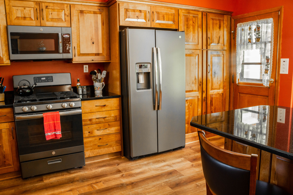 Large mountain style u-shaped medium tone wood floor and brown floor open concept kitchen photo with a farmhouse sink, raised-panel cabinets, medium tone wood cabinets, quartz countertops, stainless steel appliances, an island and black countertops