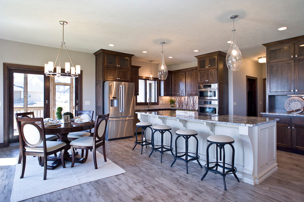 Inspiration for a mid-sized transitional l-shaped light wood floor and multicolored floor eat-in kitchen remodel with an undermount sink, raised-panel cabinets, dark wood cabinets, granite countertops, beige backsplash, glass tile backsplash, stainless steel appliances and an island