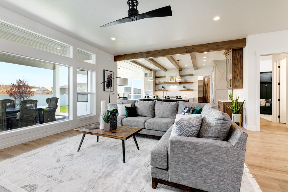 Photo of a large country open concept living room in Boise with white walls, light hardwood floors, a standard fireplace, a brick fireplace surround, a wall-mounted tv and beige floor.