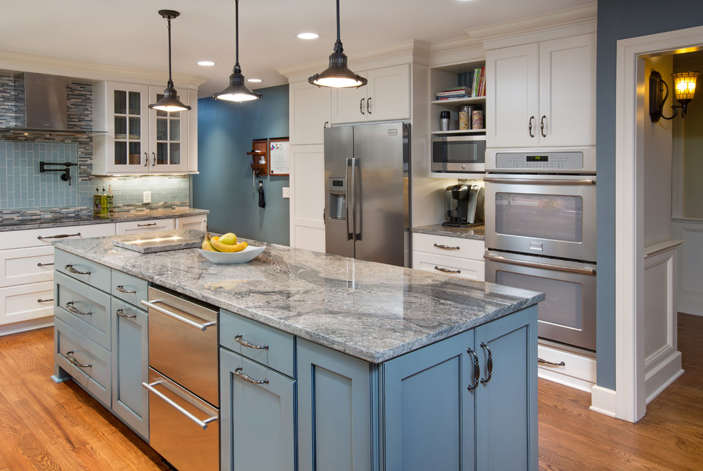Inspiration for a large transitional u-shaped kitchen in Columbus with a farmhouse sink, granite benchtops, blue splashback, glass tile splashback, stainless steel appliances, medium hardwood floors, with island, recessed-panel cabinets and blue cabinets.