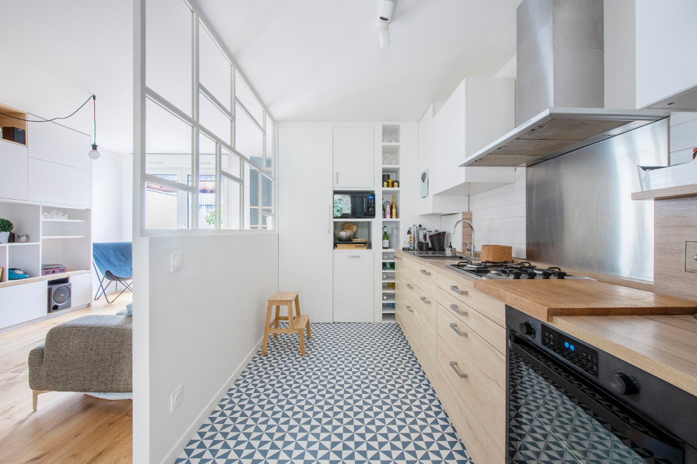 Foto på ett mellanstort nordiskt beige linjärt kök och matrum, med en nedsänkt diskho, släta luckor, skåp i ljust trä, träbänkskiva, beige stänkskydd, stänkskydd i trä, rostfria vitvaror, cementgolv och blått golv