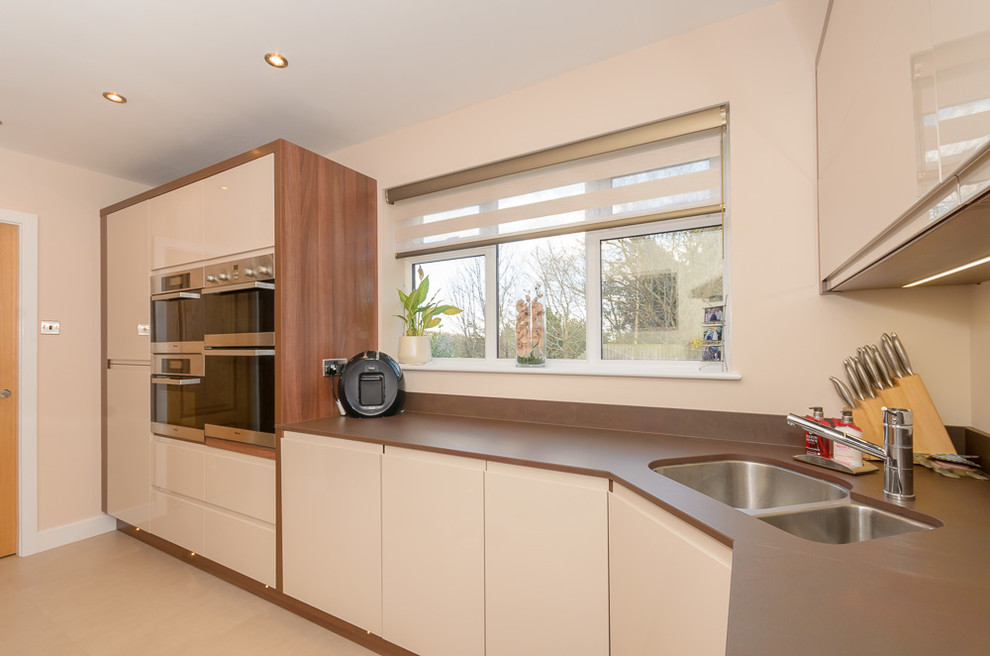 Photo of a small contemporary u-shaped eat-in kitchen in Other with an undermount sink, flat-panel cabinets, light wood cabinets, quartz benchtops, brown splashback, panelled appliances, linoleum floors and a peninsula.