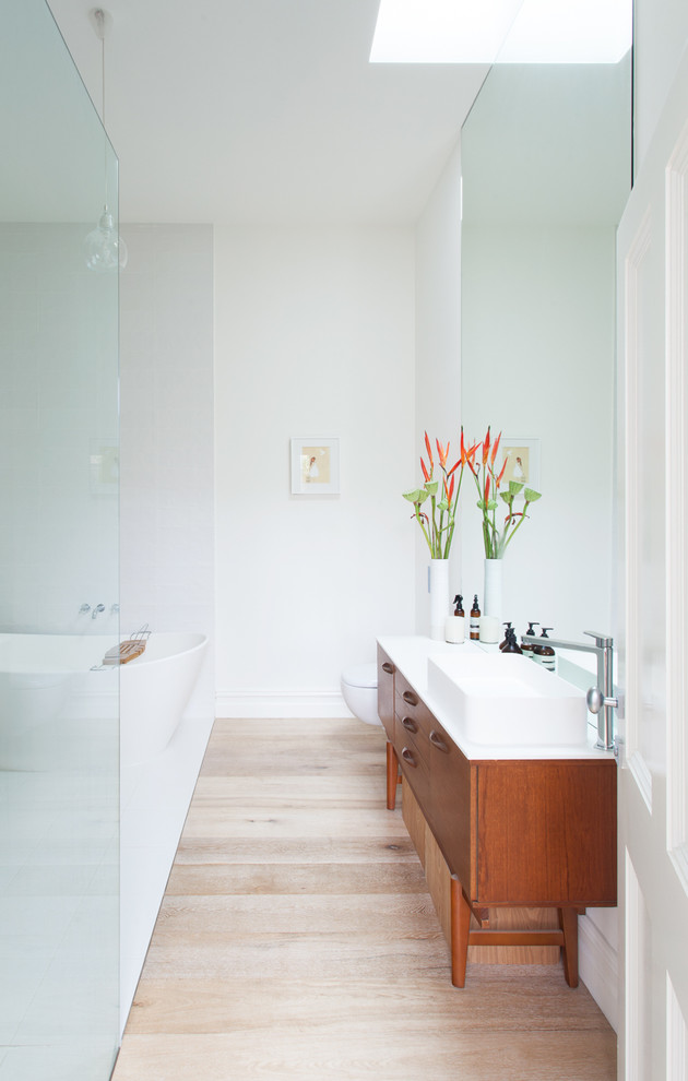 Photo of a contemporary bathroom in Melbourne with a vessel sink, medium wood cabinets, a freestanding tub, white walls, light hardwood floors and flat-panel cabinets.