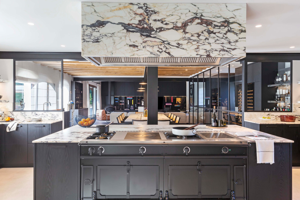 Photo of a large industrial u-shaped open plan kitchen in Paris with an undermount sink, flat-panel cabinets, black cabinets, marble benchtops, marble splashback, black appliances, ceramic floors, with island and beige floor.
