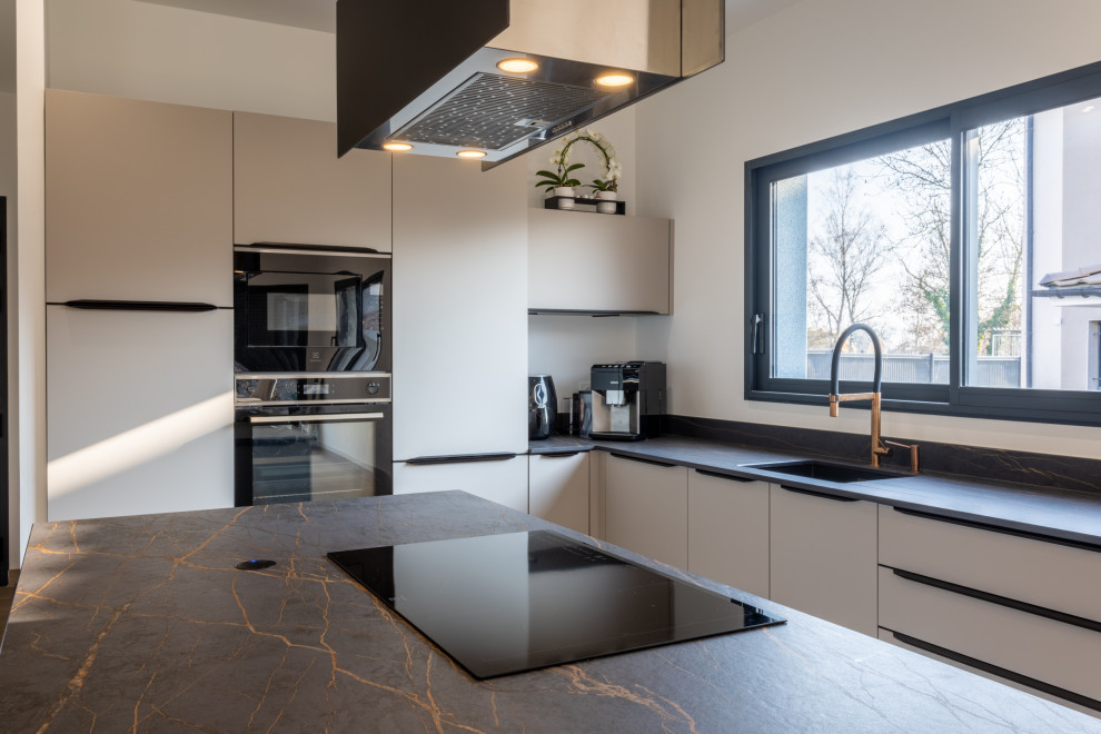 Example of a mid-sized trendy l-shaped light wood floor and brown floor open concept kitchen design in Lyon with an integrated sink, beaded inset cabinets, beige cabinets, tile countertops, black backsplash, ceramic backsplash, paneled appliances, an island and black countertops