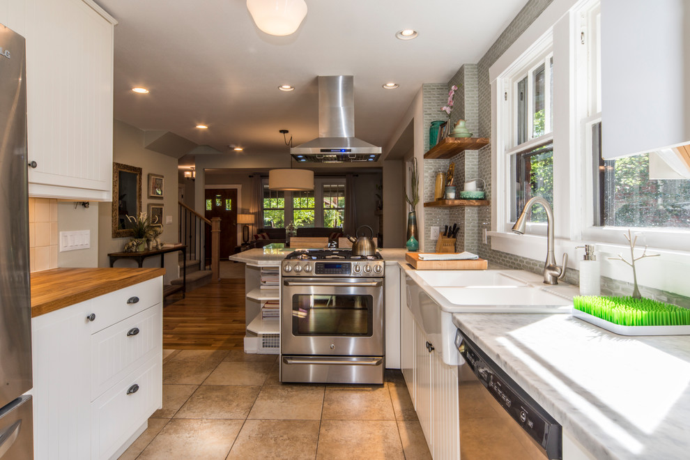Photo of a small arts and crafts l-shaped kitchen in Denver with a farmhouse sink, flat-panel cabinets, white cabinets, marble benchtops, green splashback, glass tile splashback, stainless steel appliances, porcelain floors, no island and brown floor.