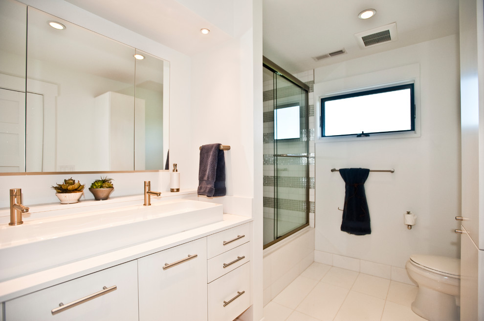 Photo of a mid-sized contemporary 3/4 bathroom with white cabinets, an alcove tub, a shower/bathtub combo, a one-piece toilet, gray tile, ceramic tile, white walls, porcelain floors, a trough sink, engineered quartz benchtops, white floor and a sliding shower screen.