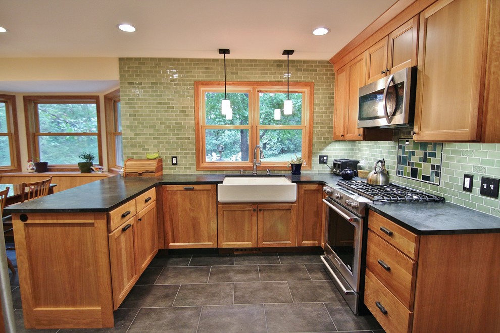 Small traditional u-shaped eat-in kitchen in Minneapolis with a farmhouse sink, flat-panel cabinets, light wood cabinets, soapstone benchtops, green splashback, ceramic splashback, stainless steel appliances, porcelain floors and a peninsula.