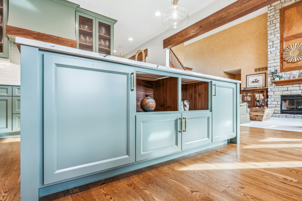 Large traditional l-shaped open plan kitchen in Columbus with an undermount sink, recessed-panel cabinets, green cabinets, quartz benchtops, white splashback, ceramic splashback, stainless steel appliances, medium hardwood floors, with island, white benchtop and exposed beam.
