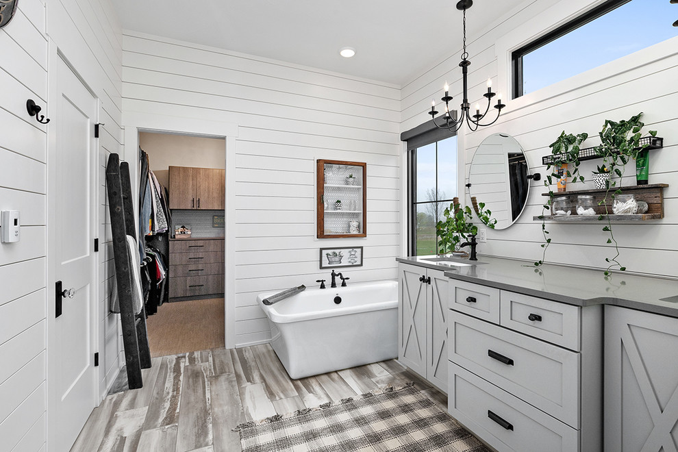 Photo of a country master bathroom in Grand Rapids with shaker cabinets, grey cabinets, a freestanding tub, white walls, an undermount sink, engineered quartz benchtops, grey floor and grey benchtops.