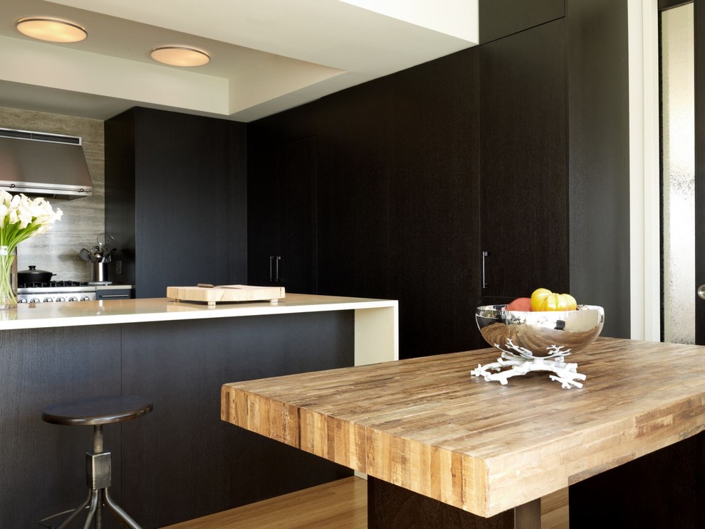 This is an example of a contemporary kitchen in New York with wood benchtops, flat-panel cabinets and black cabinets.