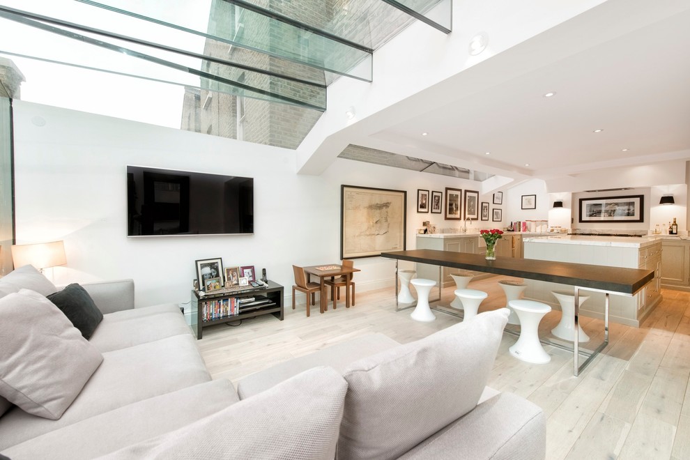 This is an example of a contemporary formal open concept living room in London with white walls, light hardwood floors and a wall-mounted tv.
