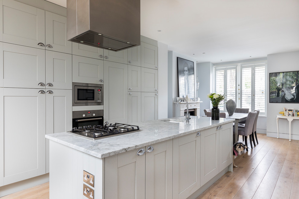 This is an example of a transitional eat-in kitchen in London with an undermount sink, shaker cabinets, grey cabinets, stainless steel appliances, light hardwood floors, with island, beige floor and grey benchtop.