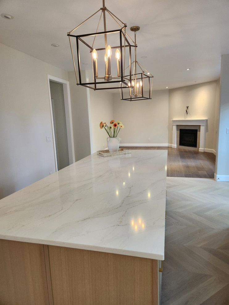 Inspiration for a large transitional light wood floor and beige floor eat-in kitchen remodel in Vancouver with a farmhouse sink, shaker cabinets, white cabinets, quartzite countertops, white backsplash, quartz backsplash, stainless steel appliances, an island and white countertops