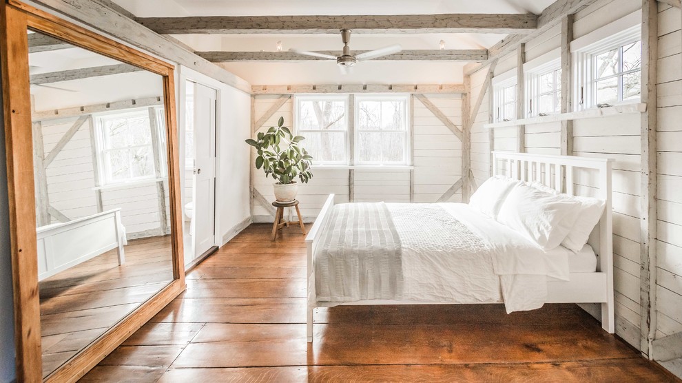 This is an example of a country bedroom in New York with white walls, dark hardwood floors and brown floor.