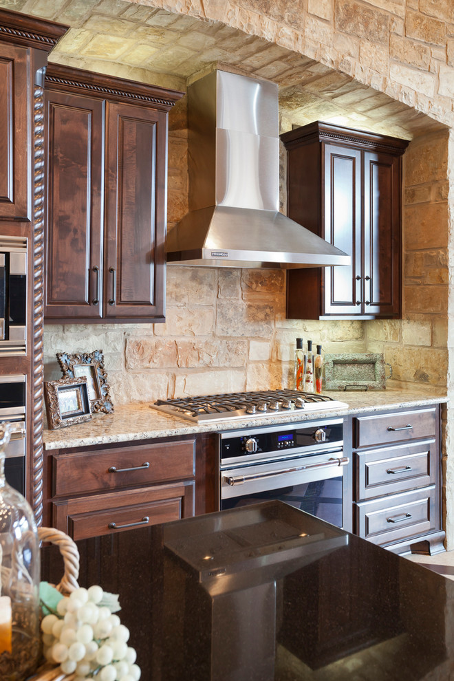 Large country kitchen in Austin with a farmhouse sink, raised-panel cabinets, dark wood cabinets, granite benchtops, stone tile splashback, stainless steel appliances and multiple islands.