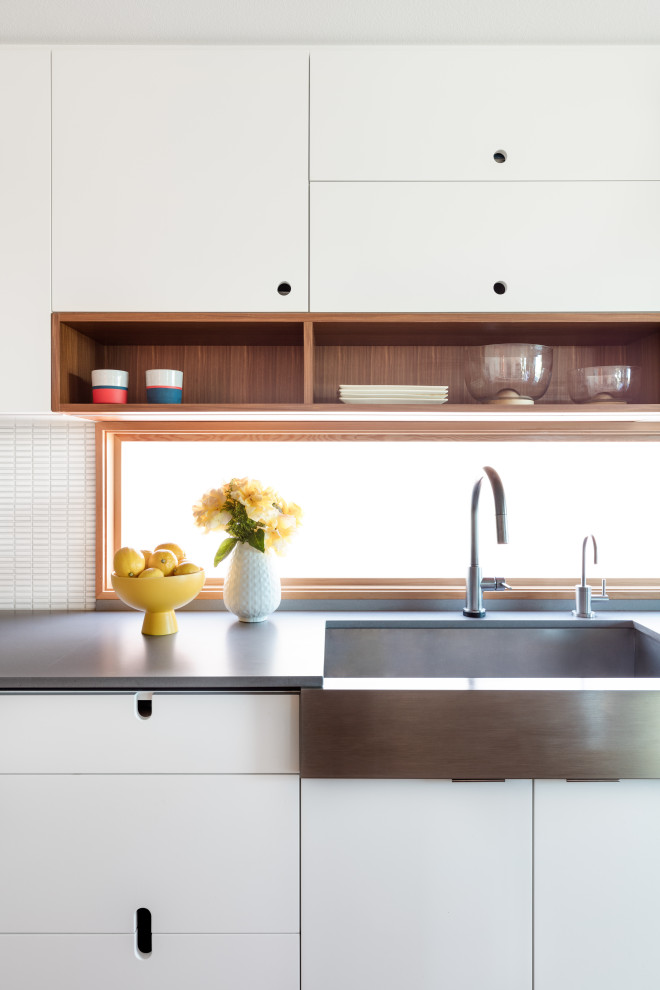 Medium sized retro galley kitchen/diner in Seattle with flat-panel cabinets, white cabinets, composite countertops, stainless steel appliances, medium hardwood flooring, an island, white worktops, a belfast sink, white splashback, mosaic tiled splashback and brown floors.