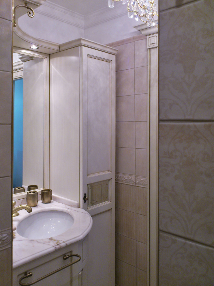 This is an example of a mid-sized transitional wet room bathroom in Moscow with recessed-panel cabinets, beige cabinets, a wall-mount toilet, beige tile, ceramic tile, beige walls, ceramic floors, marble benchtops, beige floor and a hinged shower door.