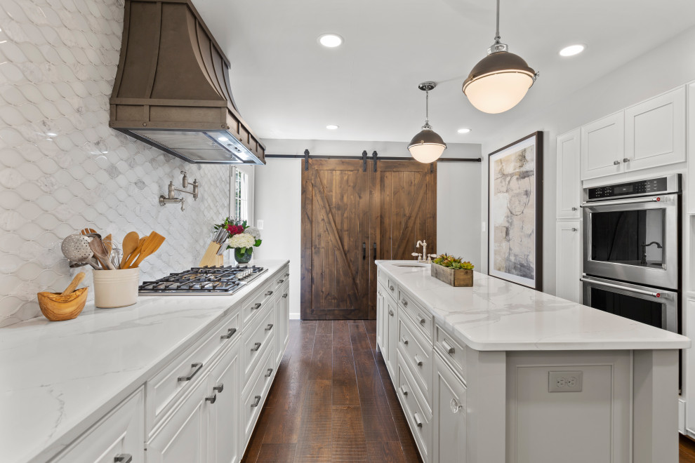 Inspiration for a mid-sized transitional single-wall dark wood floor and brown floor eat-in kitchen remodel in DC Metro with a farmhouse sink, recessed-panel cabinets, white cabinets, quartzite countertops, white backsplash, glass tile backsplash, stainless steel appliances, two islands and white countertops