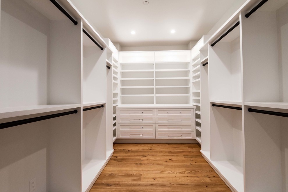 Photo of a mid-sized beach style gender-neutral walk-in wardrobe in Los Angeles with white cabinets, medium hardwood floors and brown floor.