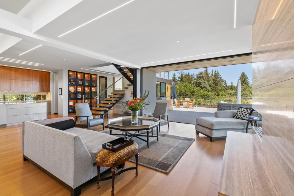This is an example of a mid-sized modern open concept living room in San Francisco with white walls, light hardwood floors, a ribbon fireplace, a stone fireplace surround and brown floor.