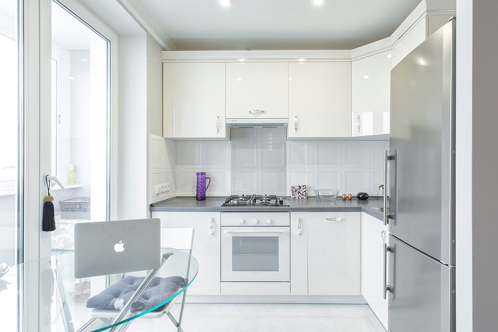 Photo of a contemporary l-shaped open plan kitchen in Moscow with a drop-in sink, flat-panel cabinets, white cabinets, white splashback, white appliances, no island and white floor.
