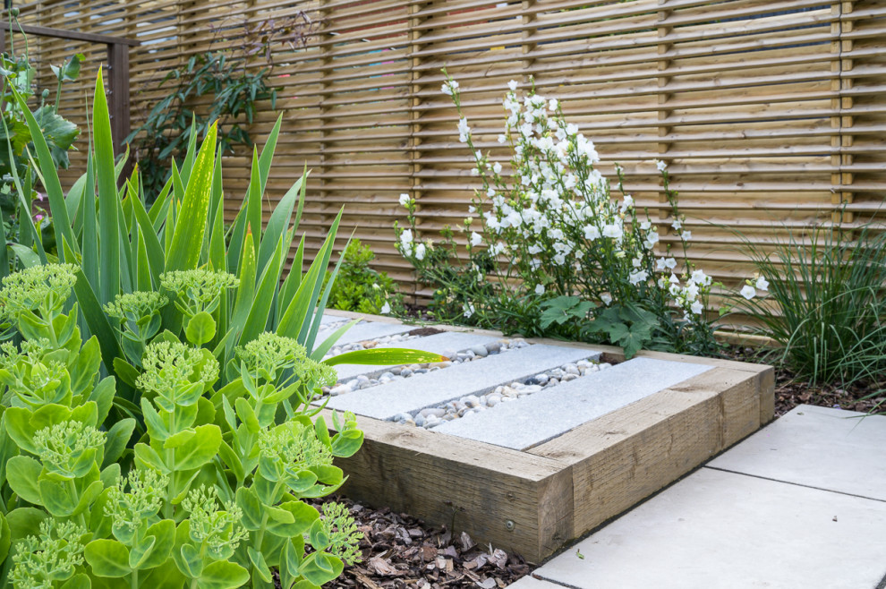 Small contemporary back garden in London with a flowerbed, decorative stones and a wood fence.