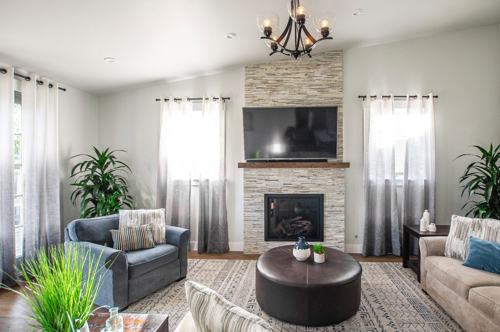 Example of a mid-sized transitional open concept medium tone wood floor, brown floor and vaulted ceiling family room design in San Francisco with gray walls, a standard fireplace, a stacked stone fireplace and a wall-mounted tv