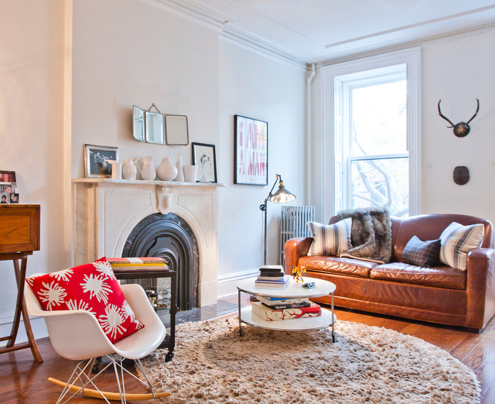 Eclectic living room in New York with white walls, medium hardwood floors and a standard fireplace.
