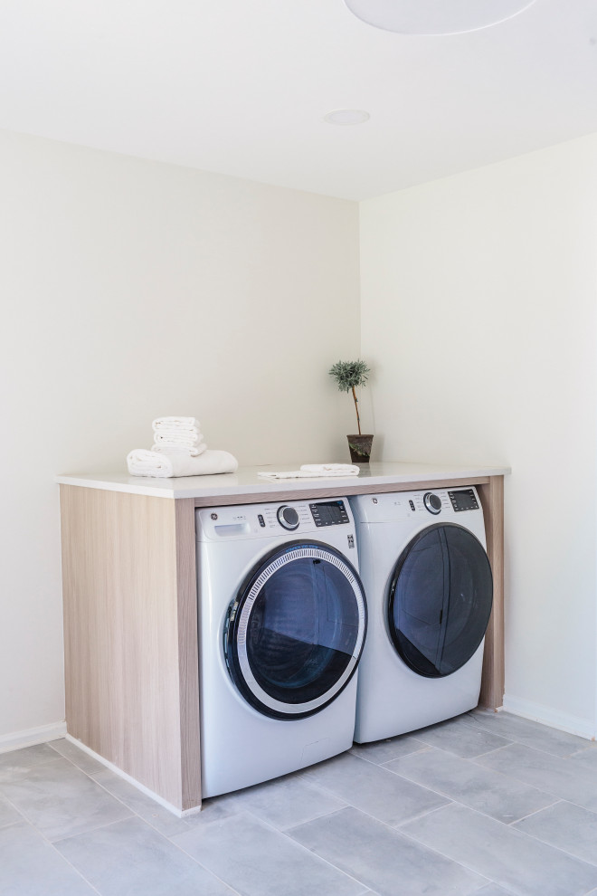 Immagine di una lavanderia multiuso design di medie dimensioni con ante lisce, ante in legno chiaro, pareti bianche, pavimento in ardesia, lavatrice e asciugatrice affiancate, pavimento grigio e top bianco
