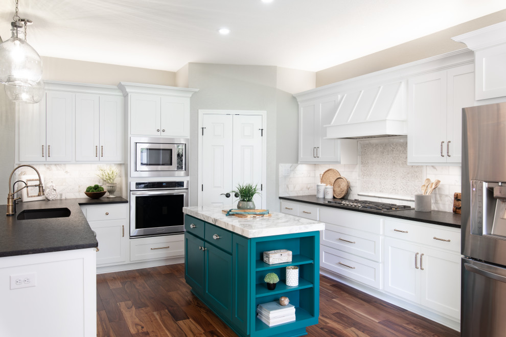 Design ideas for a mid-sized transitional l-shaped eat-in kitchen in Austin with an undermount sink, white cabinets, granite benchtops, white splashback, stainless steel appliances, light hardwood floors, with island, brown floor and multi-coloured benchtop.