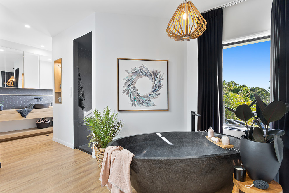 This is an example of a contemporary master bathroom in Brisbane with flat-panel cabinets, light wood cabinets, a freestanding tub, black tile, light hardwood floors, a vessel sink, wood benchtops, beige floor and beige benchtops.