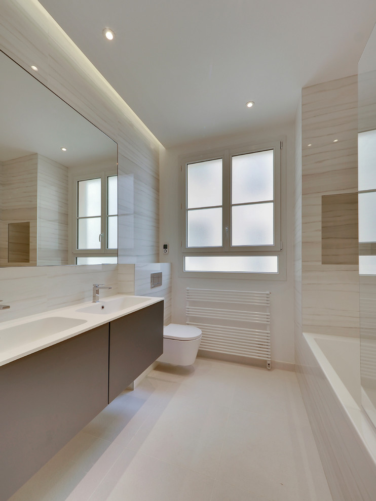 Mid-sized transitional 3/4 bathroom in Paris with an undermount tub, a wall-mount toilet, white tile, ceramic tile, white walls, ceramic floors, a console sink, stainless steel benchtops, white floor and white benchtops.