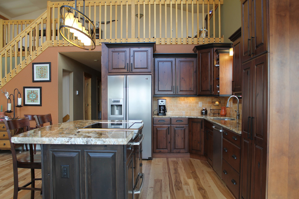 Large mountain style l-shaped light wood floor open concept kitchen photo in Denver with an undermount sink, raised-panel cabinets, dark wood cabinets, granite countertops, beige backsplash, stone tile backsplash, stainless steel appliances and an island