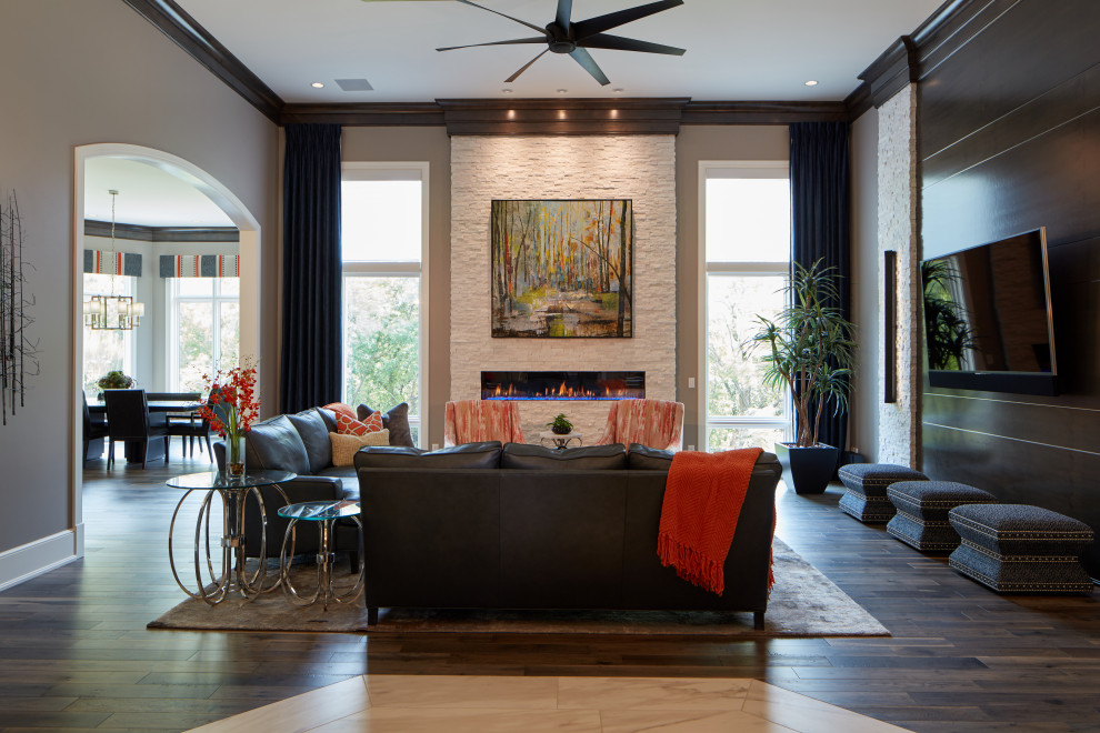 This is an example of an expansive transitional open concept living room in Omaha with medium hardwood floors, a ribbon fireplace, a stone fireplace surround, a wall-mounted tv, brown floor and grey walls.