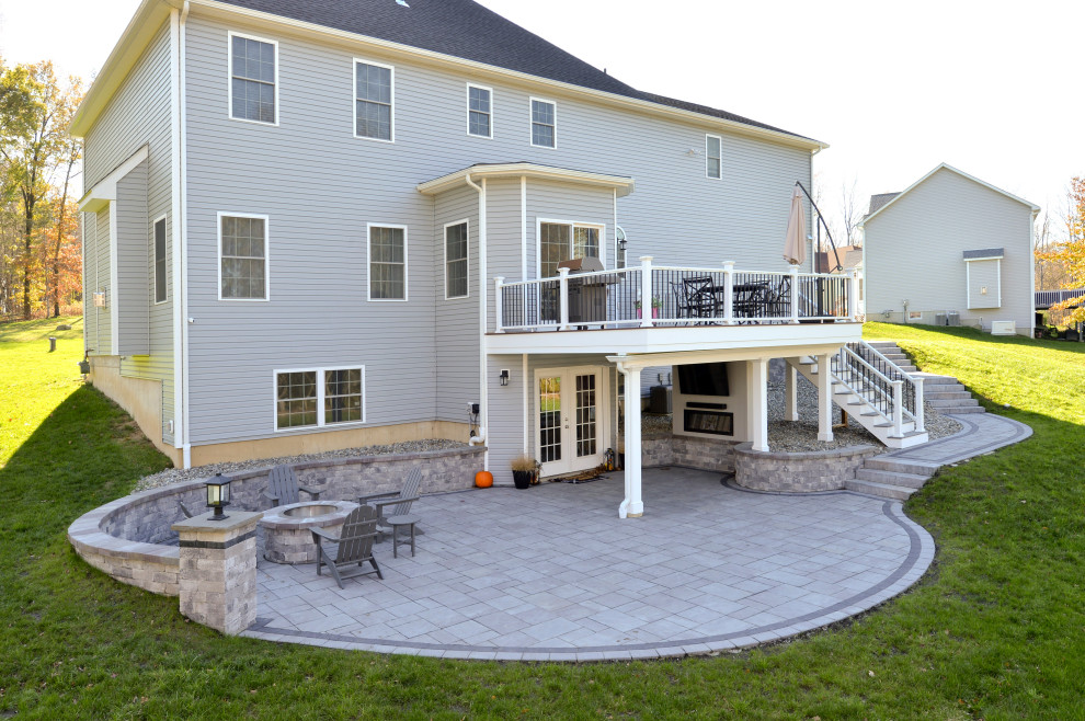 Exempel på en stor modern terrass på baksidan av huset, med en eldstad och räcke i flera material