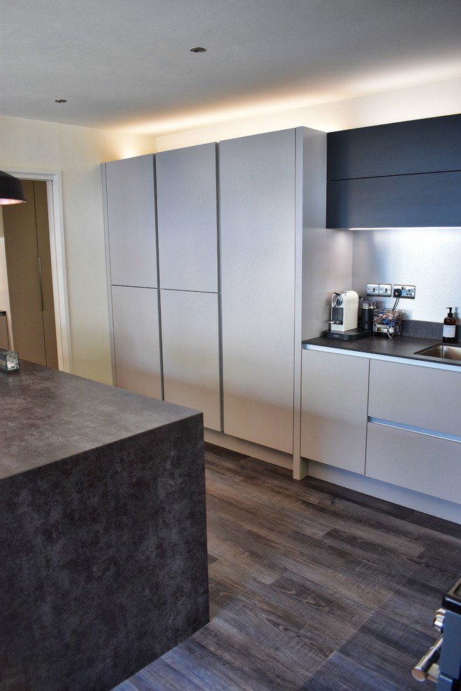 Inspiration for a large contemporary eat-in kitchen in Cambridgeshire with an undermount sink, flat-panel cabinets, beige cabinets, black appliances, light hardwood floors, with island and grey benchtop.