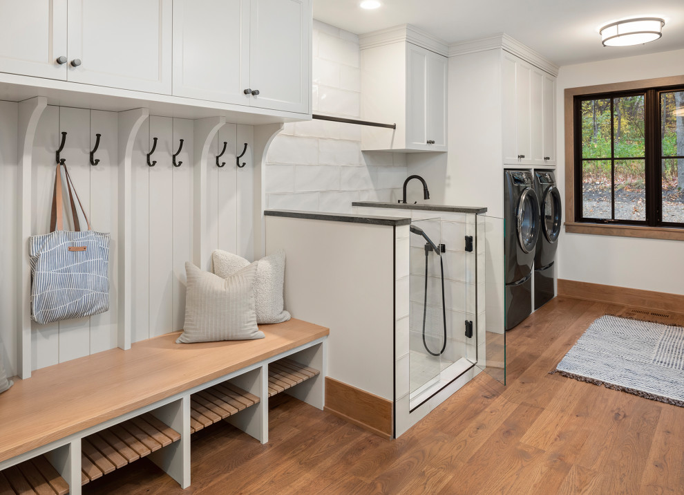 Photo of a mid-sized beach style single-wall utility room in Minneapolis with an undermount sink, recessed-panel cabinets, beige cabinets, white splashback, ceramic splashback, white walls, medium hardwood floors, a side-by-side washer and dryer and brown floor.
