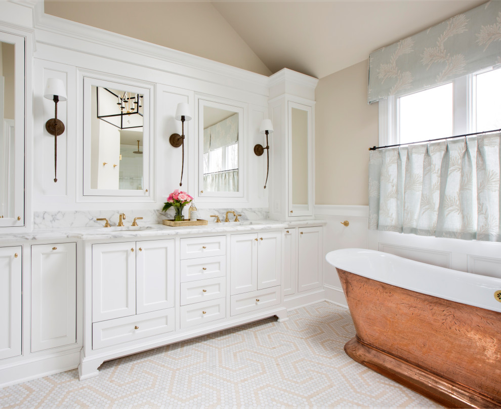 This is an example of a large traditional master bathroom in New York with recessed-panel cabinets, white cabinets, a freestanding tub, an alcove shower, a two-piece toilet, white tile, ceramic tile, beige walls, marble floors, an undermount sink, marble benchtops, beige floor, a hinged shower door, white benchtops, an enclosed toilet, a double vanity, a built-in vanity, vaulted and decorative wall panelling.